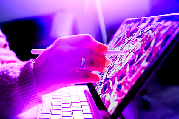 A hand holding a stylist and working on a computer. There is a purple overlay.