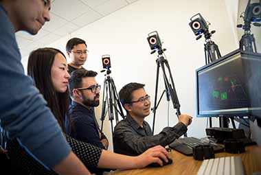 4 students and a professor looking at a computer lab monitor and discussing