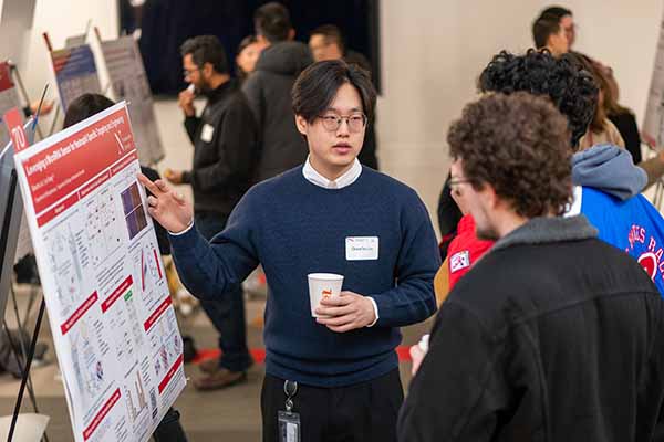 student at research expo pointing to poster as he explains to attendee his research