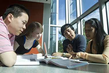 students and tutor working together at desk with computer