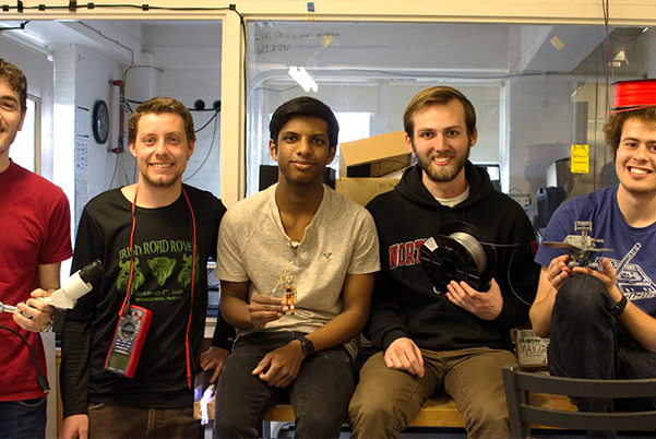students sitting on table in a row each folding parts of wireless devices such as a roll of wire